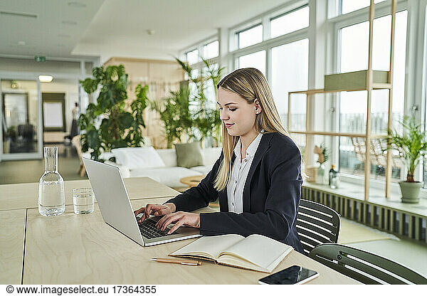 Blond trainee using laptop while sitting at desk in office