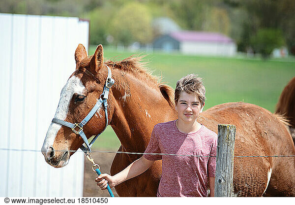 Blond tween boy leading a brown horse with white blaze.