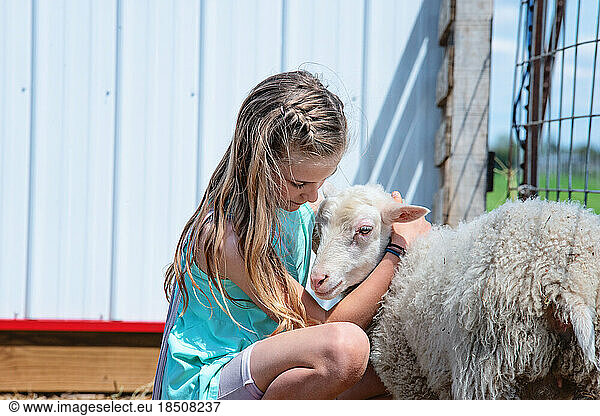Blond tween girl hugging a lamb in farmyard.