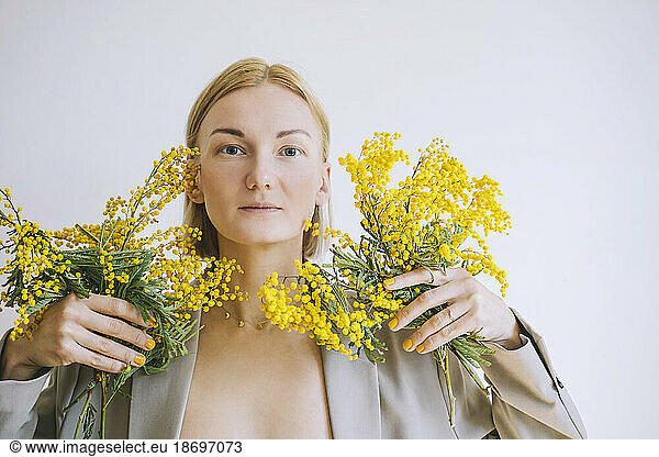 Blond woman holding bunch of mimosa flowers against white background