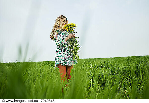 Blond woman holding flowers while standing on grass