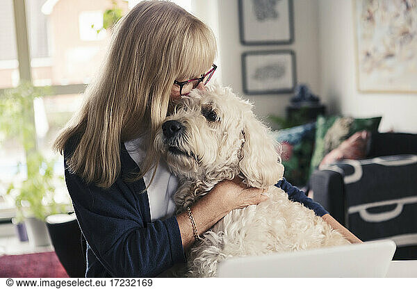 Blond woman kissing and embracing dog at home