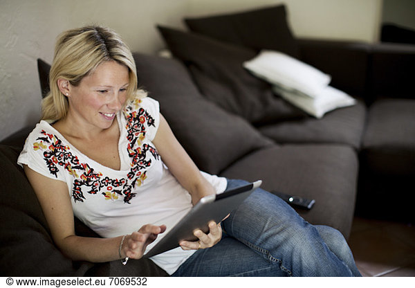 Blond woman looking at digital tablet on sofa