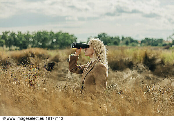 Blond woman looking through binoculars in wheat field