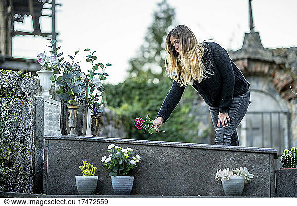 Blond woman putting flower on grave at cemetery