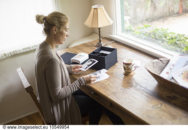 Blond woman sitting at a desk by a window  looking at photographs.