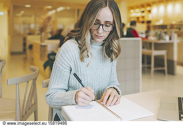 Blond woman sitting in a cafe and writing into notepad