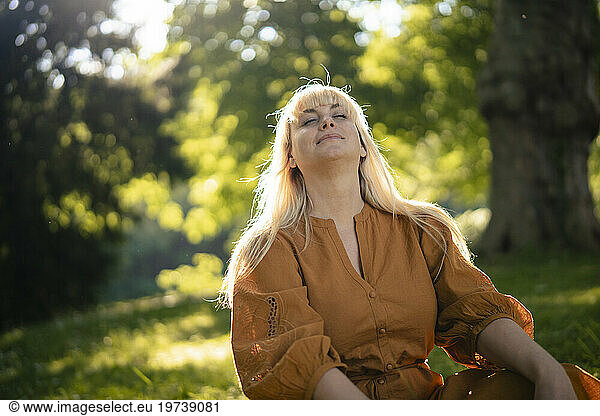 Blond woman sitting with eyes closed in park