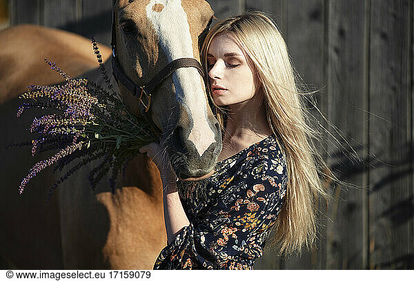 Blond woman stroking horse against old wooden wall