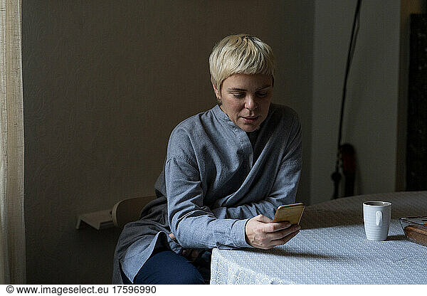Blond woman using mobile phone sitting on chair at home