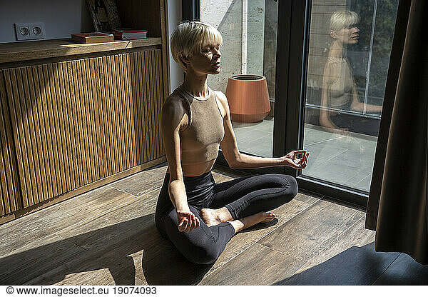 Blond woman with eyes closed meditating on floor at home