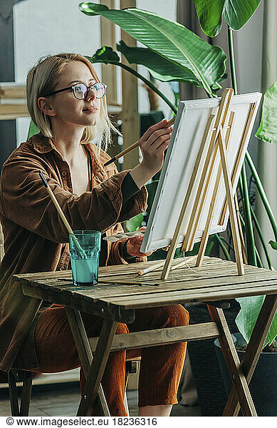 Blond woman with paintbrush painting on canvas