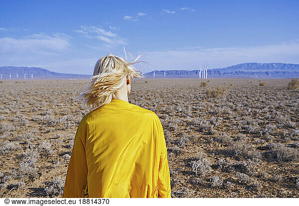 Blond woman with yellow raincoat standing in desert