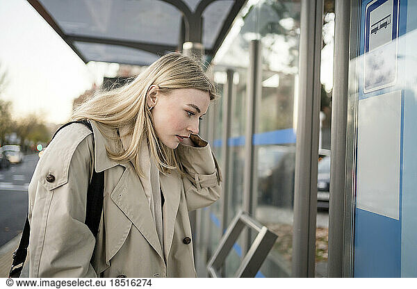 Blond young woman checking bus schedule at station