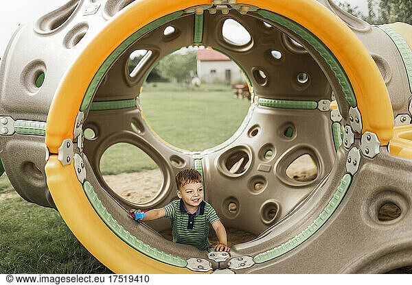Blonde boy playing inside playground equipment