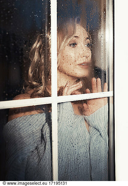 Blonde Frau hinter dem nassen Fenster