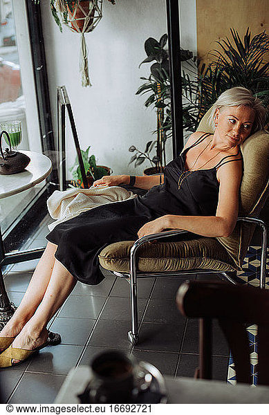 Blonde Frau in schwarzem Kleid sitzt in entspannter Position und schaut weg