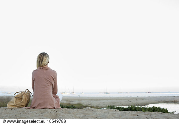 Blonde Frau sitzt an einem Sandstrand.