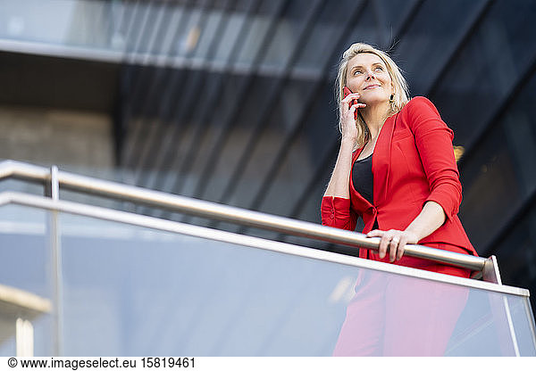 Blonde Geschäftsfrau in rotem Anzug und mit Smartphone