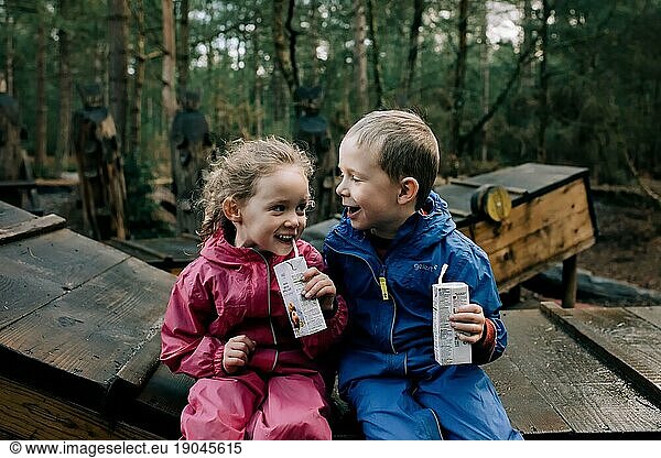 blonde girl and boy laughing drinking juice whilst outside playing