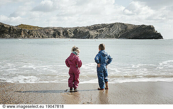blonde girl and boy standing on the shore looking at the sea thinking