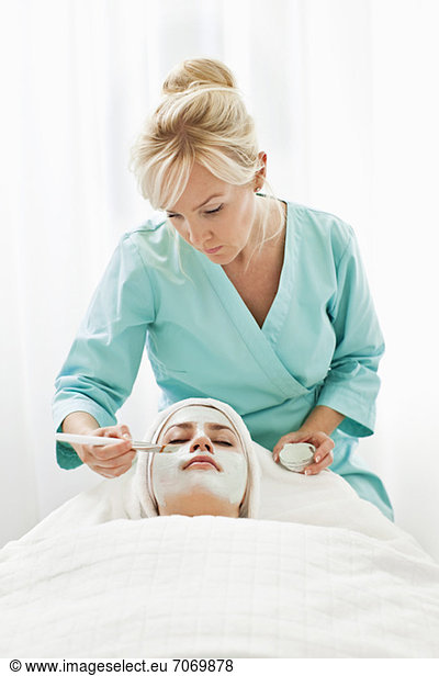 Blonde Kosmetikerin mit Gesichtsmaske für junge Kunden im Beauty Spa