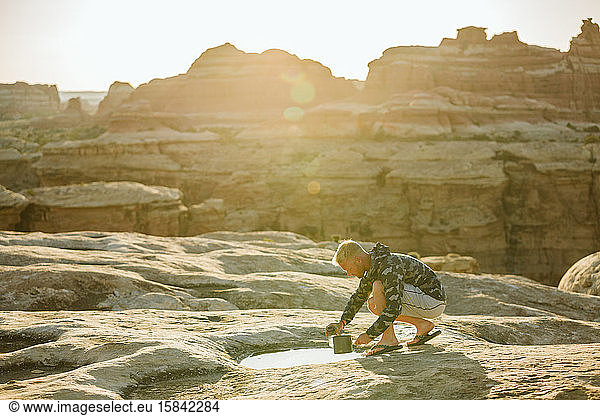 blonde man in camouflage jacket collects water from a puddle in desert