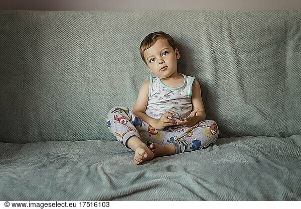 Blonde small boy with blue eyes sitting on sofa indoors