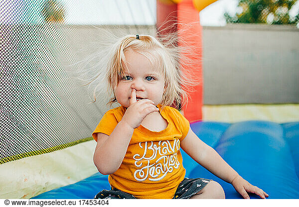 Blonde toddler girl picks nose while playing on jump house in backyard