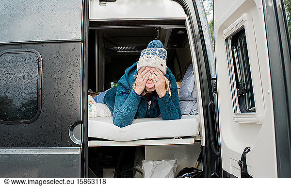 blonde woman hiding pulling silly faces in a camper van camping