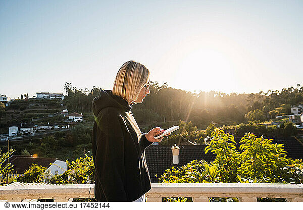 blonde woman looking at the mobile on a gazebo against sunset