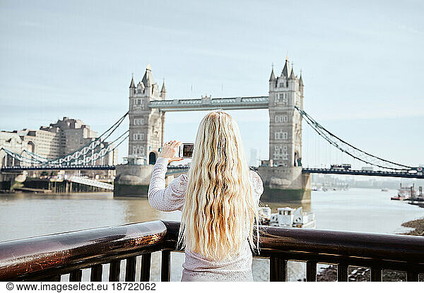 Blonde woman with wavy hair taking picture of Tower Bridge