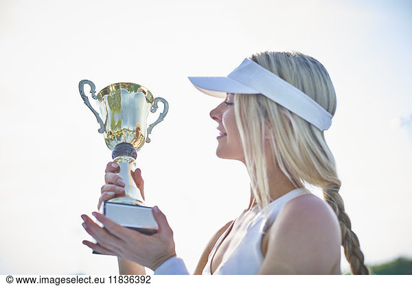 Blonde young female tennis player in visor holding championship trophy