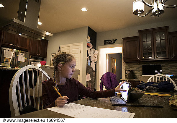 Blondes Mädchen am Küchentisch erledigt Schularbeiten am Tablet-Computer