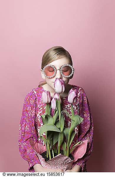 Blondes Tween Girl mit Sonnenbrille riecht an rosa Tulpen auf rosa Hintergrund