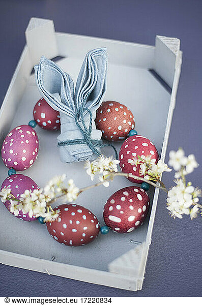 Blossoming twigs  napkin folded into shape of rabbit ears and wreath made of red spotted Easter eggs