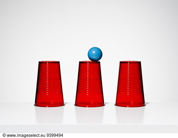 Blue ball balancing on middle of three red cups