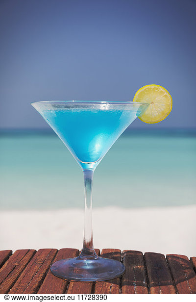 Blue cocktail with lemon slice in martini glass on sunny tropical beach