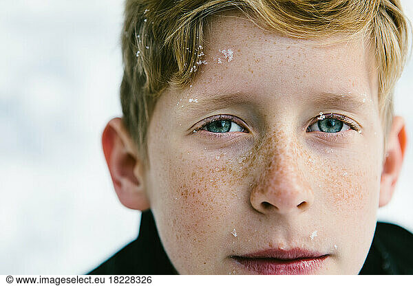 Blue eyed boy with freckles and snow flakes on his face
