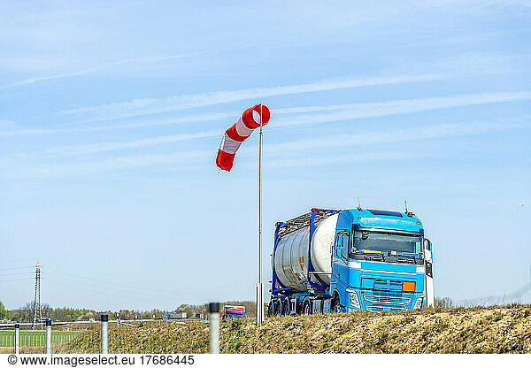 Blue fuel truck on motorway in front of windsock