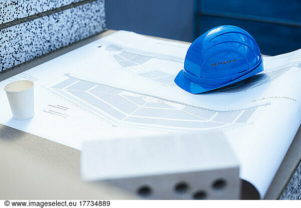 Blue hardhat and disposable cup on blueprint at construction site