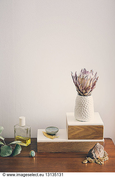 Blumenvase mit Schmuck und Schönheitsprodukten auf Tisch vor weißer Wand