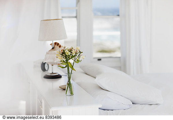 Blumenvase und Lampe im weißen Schlafzimmer