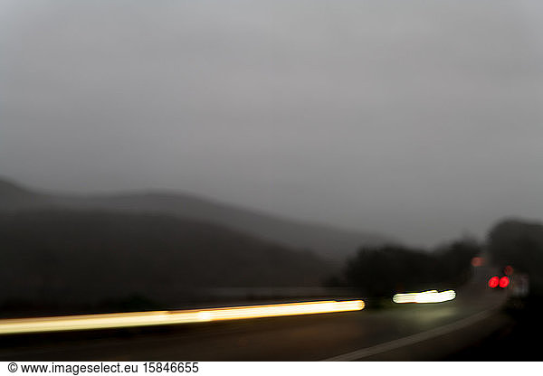 Blurred car headlights traveling down highway backed by misty hill