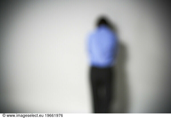 Blurred  defocused  rear view of a person standing in front of a blank wall.