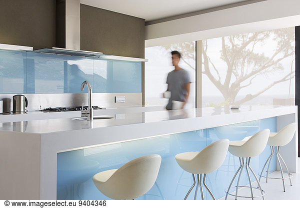 Blurred motion man walking through white and blue modern kitchen