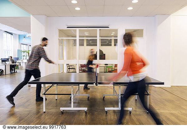 Blurred motion of business people playing table tennis in creative office