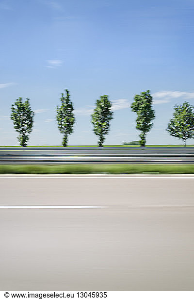 Blurred motion of trees against blue sky seen through car window