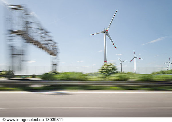 Blurred motion of windmills on landscape against sky seen through car window