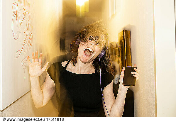 Blurred motion of woman with headphones dancing by walls at home